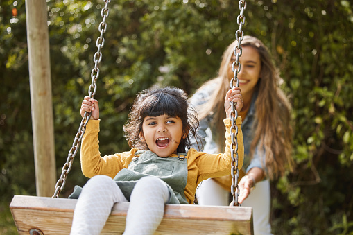 Happy, swing and mother and child in park for playing, bonding and having fun together outdoors. Nature, weekend and mom push little girl in playground for relaxing, childhood and happiness in summer