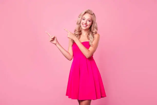 Photo of Photo of gorgeous lovely sweet lady wear bright dress demonstrate empty space recommend night club party isolated on pink color background
