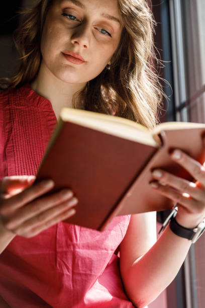 istock Young woman sitting by the window, enjoying reading a book 1707784414