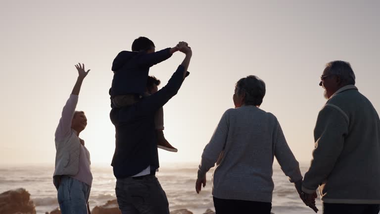 Happy family, holding hands or grandparents at beach for sunset to relax with love or care on holiday vacation. Dad, mom or back of child bonding with grandmother or grandfather at sea for ocean view