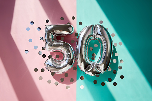 Silver numbers 50 fifty years balloons among confetti in sunlight on pink turquoise background celebration party. Greetings and congratulation