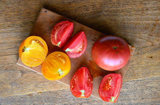 Cut up home grown heirloom tomatoes. Cherry wood cutting board on antique walnut wood table.