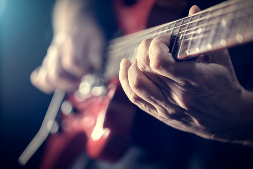 A pick strums the strings of a guitar in blue backlighting