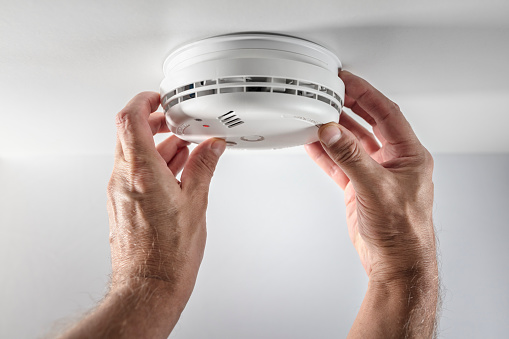 Home smoke and fire alarm detector man installing, maintenance, checking, testing or replacing battery