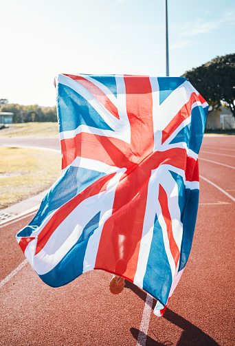 British flag, athlete running and race winner in celebration, sport achievement and training exercise on track. UK banner, victory and patriotism of person to support country in success of champion