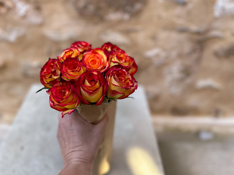 Hand holding a bouquet of reddish and orange roses