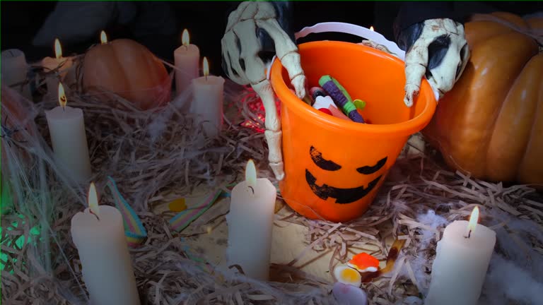 Among burning candles in barn, bone hands show a bucket of sweets collected at the holiday Happy Halloween,