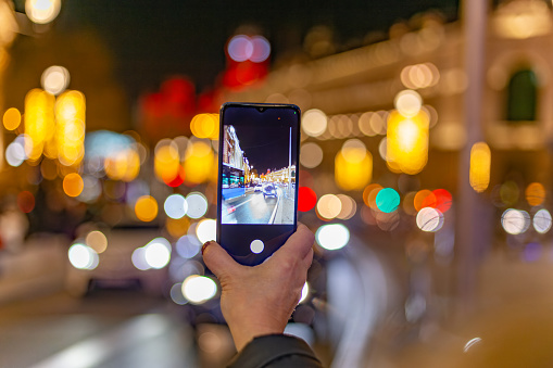 Madrid, Spain. Woman's hand photographing the Alcalá street in Madrid, Spain, at night with her mobile phone.