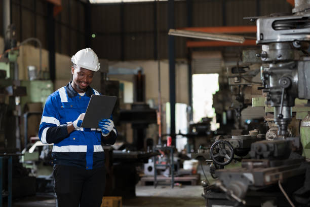 männlicher ingenieurarbeiter mit digitalem tablet während der arbeit mit drehmaschine in industriefabrik, trägt sicherheitsuniform, helm. männlicher techniker, der teile der maschine in der werkstatt wartet - cnc vehicle part quality control industry stock-fotos und bilder