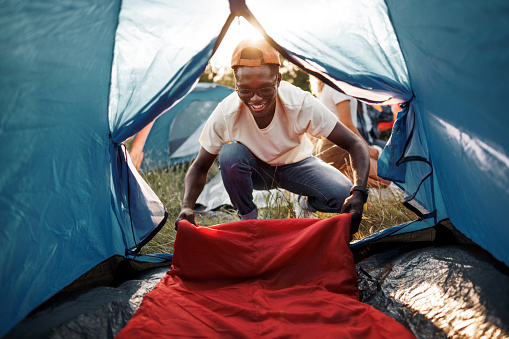 Young smiling man setting up sleeping bag in camping tent