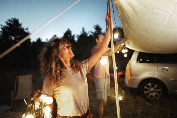 istock Young couple setting up string lights to decorate and lighten their camping spot at night 1707931931