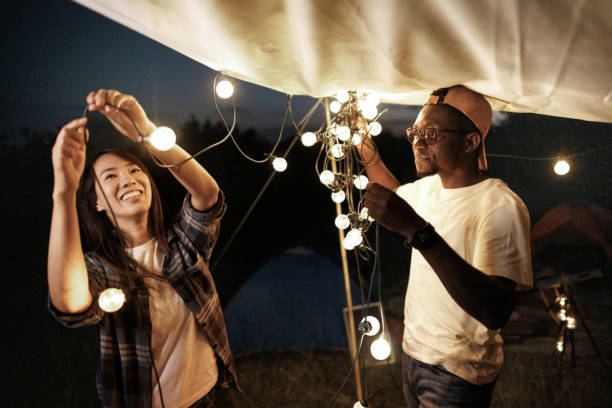 istock Young couple setting up string lights to decorate and lighten their camping spot at night 1707931949