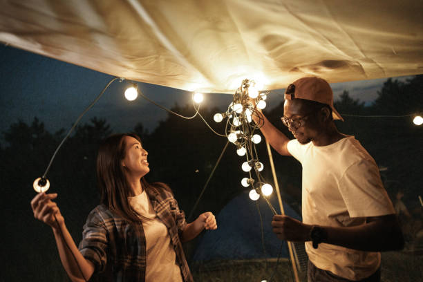 istock Young couple setting up string lights to decorate and lighten their camping spot at night 1707931955