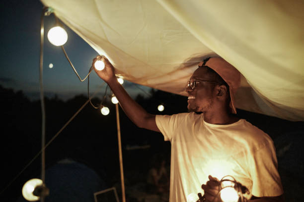 Young casually clothed man setting up string lights on his tent at night