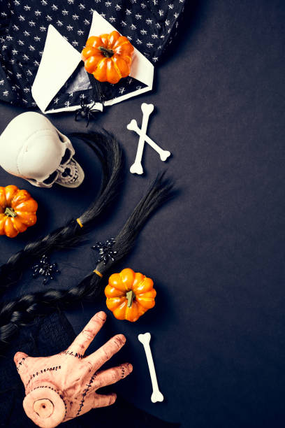 istock Halloween elements on dark background. Wednesday series style. Flat lay skull, pumpkins, wig hairs, bones, dress on black table. 1707941108