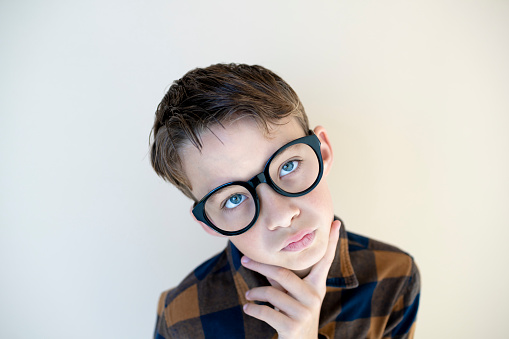 cool young boy wearing black glasses in front of brown background