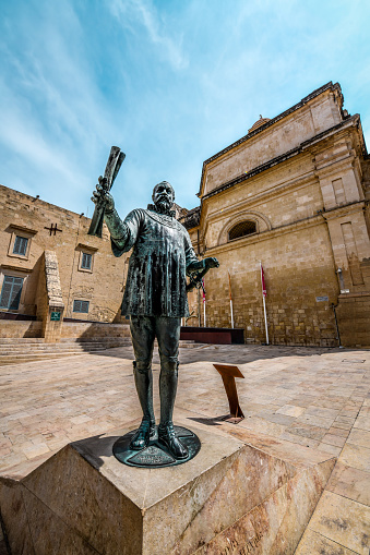 Low Angle View of Monument to Grandmaster Jean De Vallette in Valetta, Malta. In 2012, a square was inaugurated in Valletta named Pjazza Jean de La Valette which also features a statue of the Grandmaster. The statue is 2.5m high and was cast in bronze by the local sculptor Joseph Chetcuti. In the statue, La Valette is shown in armour and holding Valletta’s plan in one hand and a sword in the other.