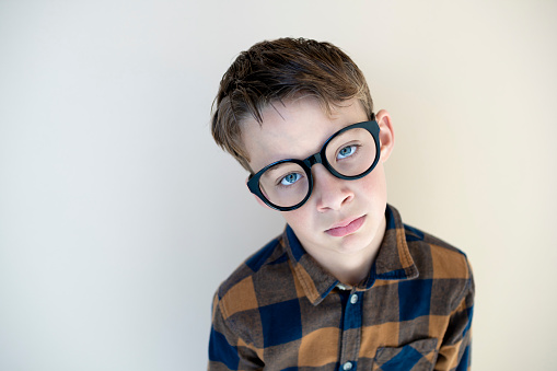 cool young boy wearing black glasses in front of brown background