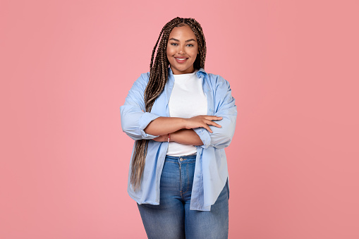 Smiling Black Overweight Lady Standing In Studio On Pink Background. Female Posing Wearing Casual Plus Size Clothes Looking At Camera. Female Beauty And Body Positive Concept