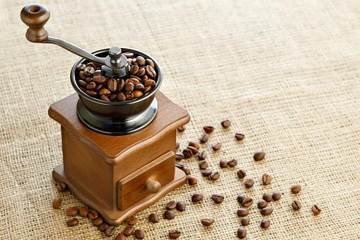 coffee beans in wooden manual grinder on table with burlap
