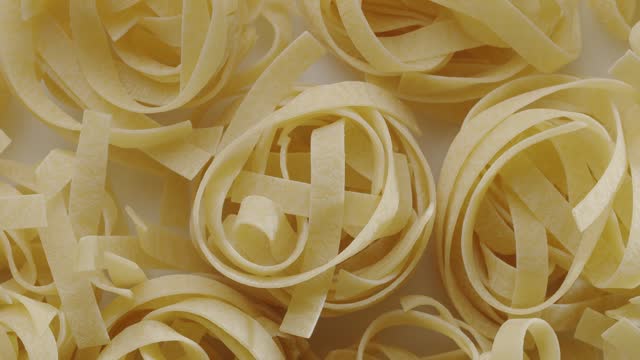 Appetizing Italian noodles in “nests” slowly move in the frame. Beautiful pasta background in Italian Mediterranean food concept.