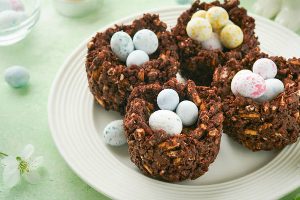 istock Easter chocolate nest cake with mini chocolate candy eggs with blossoming cherry or apple flowers on green background table. Creative recipe for Easter table with holiday decorations. Top view. 1707991643