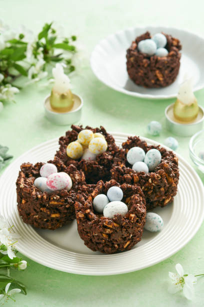 istock Easter chocolate nest cake with mini chocolate candy eggs with blossoming cherry or apple flowers on green background table. Creative recipe for Easter table with holiday decorations. Top view. 1707991794
