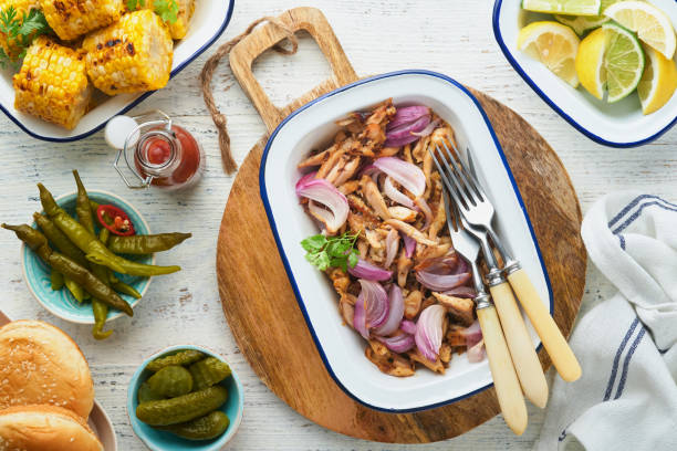 istock Pulled bbq chicken with baked onions on serving platter, bbq corn, pickles, chili peppers and buns for hot dogs and burgers, tomato sauce. Traditional American grilled summer bbq sandwiches dishes. 1707992124