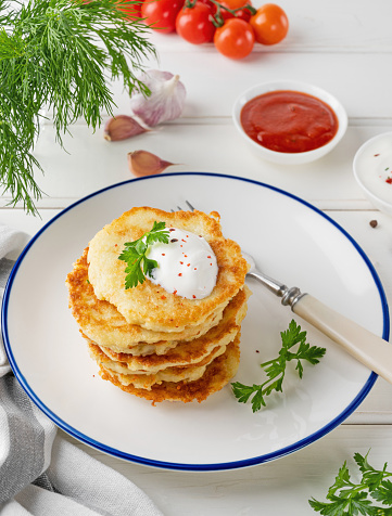 Potato pancakes, latkes or draniki with fresh herbs and sour cream on a plate on a white wooden background. Top view, copy space