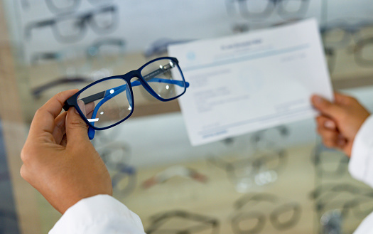 Close-up on an eye doctor holding glasses and a prescription at the optician's shop