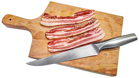Boiled pork bacon slices, cut with a large stainless steel Chef's knife, on a wooden chopping board, isolated on white background, high resolution stock photo.