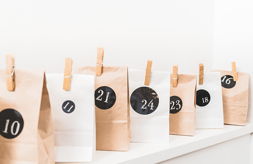Handmade advent calendar with paper bags and stickers, standing on a white wooden board