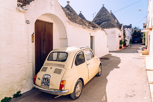 Alberobello, Italy - March 9, 2019: Old Fiat 500 car parked at the door of a house between Italian trullis.