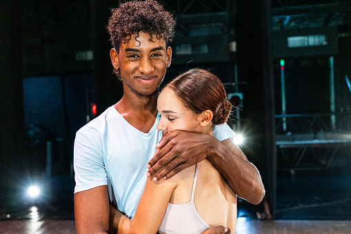 Portrait of a young ballet friends embracing at stage theater