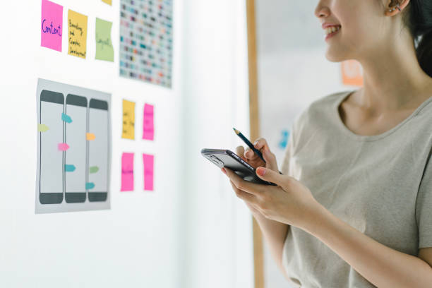Creative ux designer brainstorming designing screens for mobile responsive website development with UI UX. Developing wireframe sketch layout design mockup on smartphone screen.