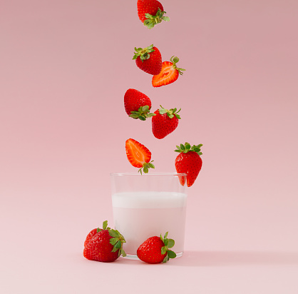 Creative layout made of strawberries falling into glass cup of milk drink with strawberry taste on pastel pink background. Minimal smoothie or milkshake concept. Healthy food for breakfast and snack.