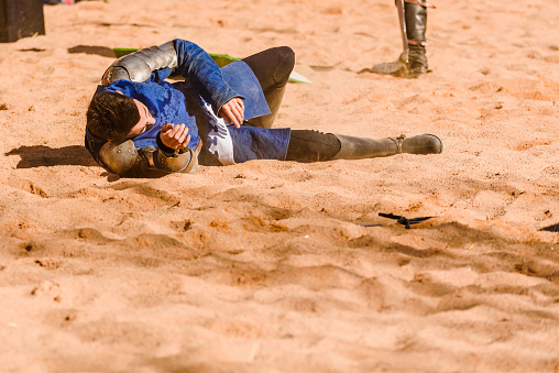 Valencia, Spain - January 27, 2019: An actor disguised as a Medievale knight lying on the ground defeated after a sword battle in a performance during a medieval spring festival.