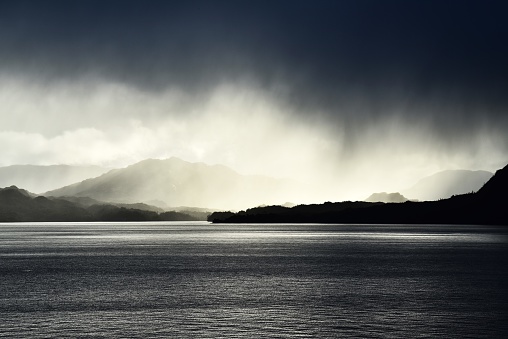 Rain falls from dark clouds with the landscape of Chile's fjords region in the background.