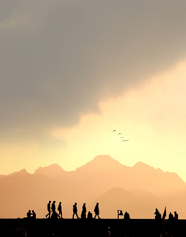 Silhouetted people relaxing in old town marina over sunset sky and high mountains in Antalya, Turkey