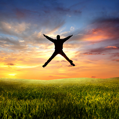 One young man jumping on green landscape during sunset