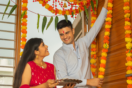 Low angle view of happy young couple decorating floral garlands on wooden door at home during festival