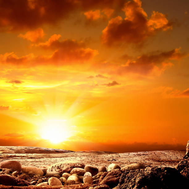 Conceptual image of dried and cracked landscape over red sunset sky with sun