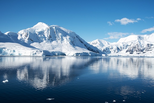 On a rare clear day, snowy mountains are reflected in the placid  waters of a tranquil cove in the Antarctic Peninsula.