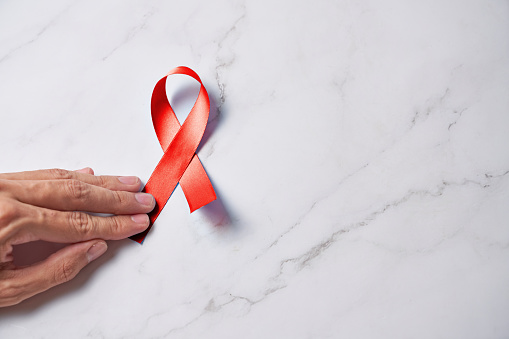 Woman hands with AID red ribbon a symbol of the fight against HIV, AIDS and cancer.
