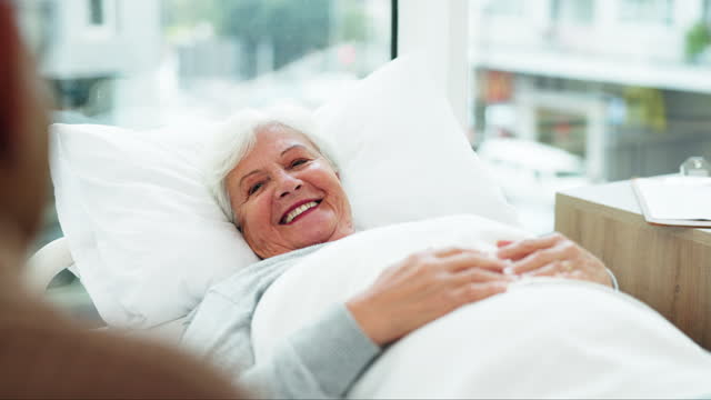 Happy, senior woman and bed in hospital, clinic and talking to therapist, doctor or specialist in healthcare, medicine or care. Elderly person, smile and laugh with medical nurse or nursing home