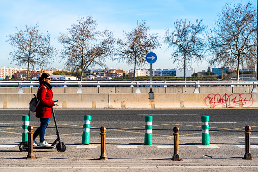 Valencia, Spain - February 28, 2019: Woman moving on her electric scooter transiting a bicycle lane isolated from other vehicles for safety and sustainability.