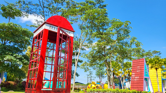 Banyuwangi, Indonesia - May 23, 2023. red vintage phone booth in the park area with blue sky background.
