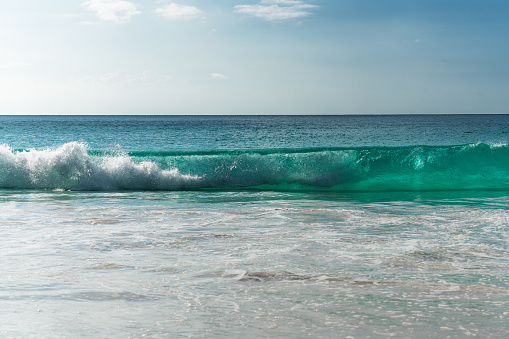 Turquoise wave breaks on sandy beach in Seychelles.
