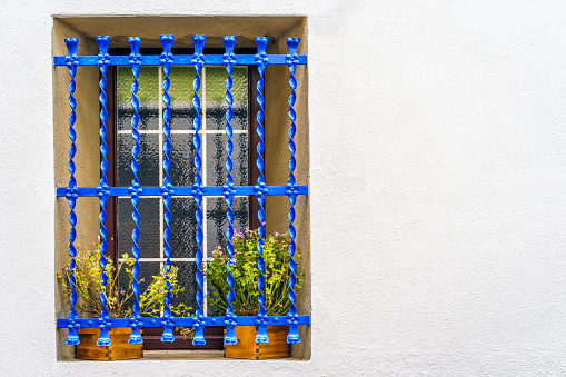 Wooden window with flower pots behind blue metal railings on a white facade