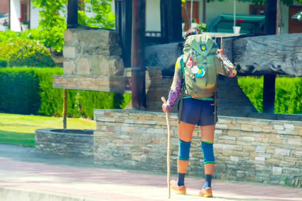 Rear view of pilgrim walking along the  'camino de santiago' with backpack and scallop shell symbols, walking cane and knee braces in old town Villafranca del Bierzo, León province, Castilla y León, Spain, Camino de Santiago.